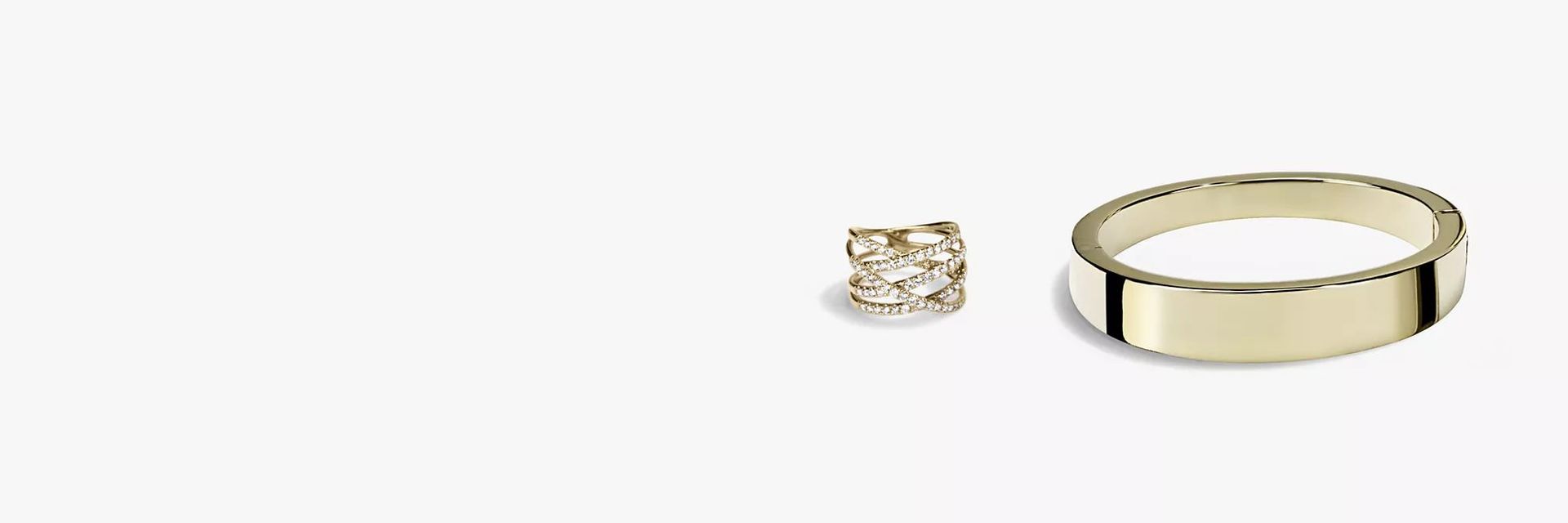 A diamond wrap yellow gold fashion ring lying next to a thick yellow gold bracelet.